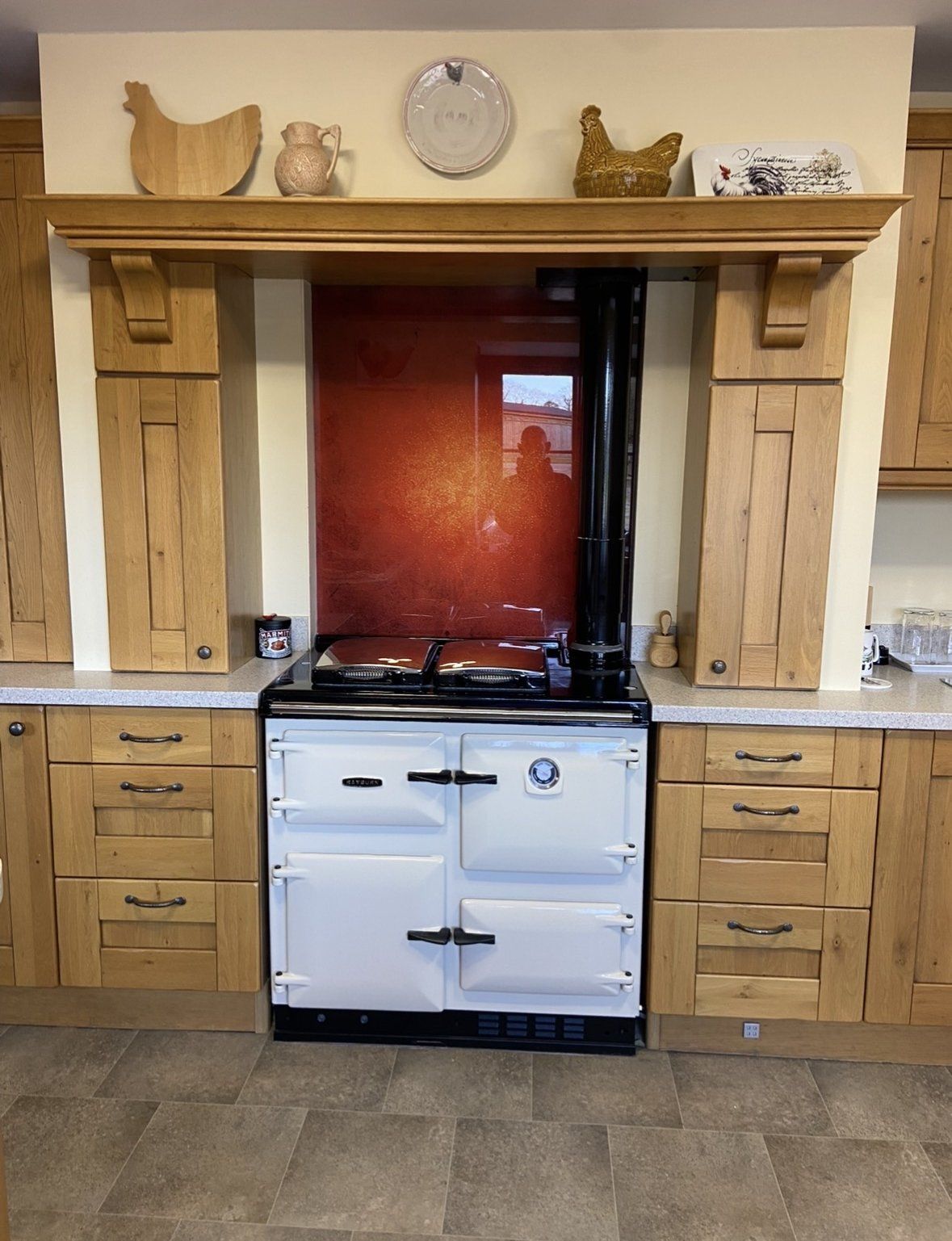 A new cream Rayburn 480K fitted between oak kitchen cabinets, with a red glass splashback and a black flue pipe