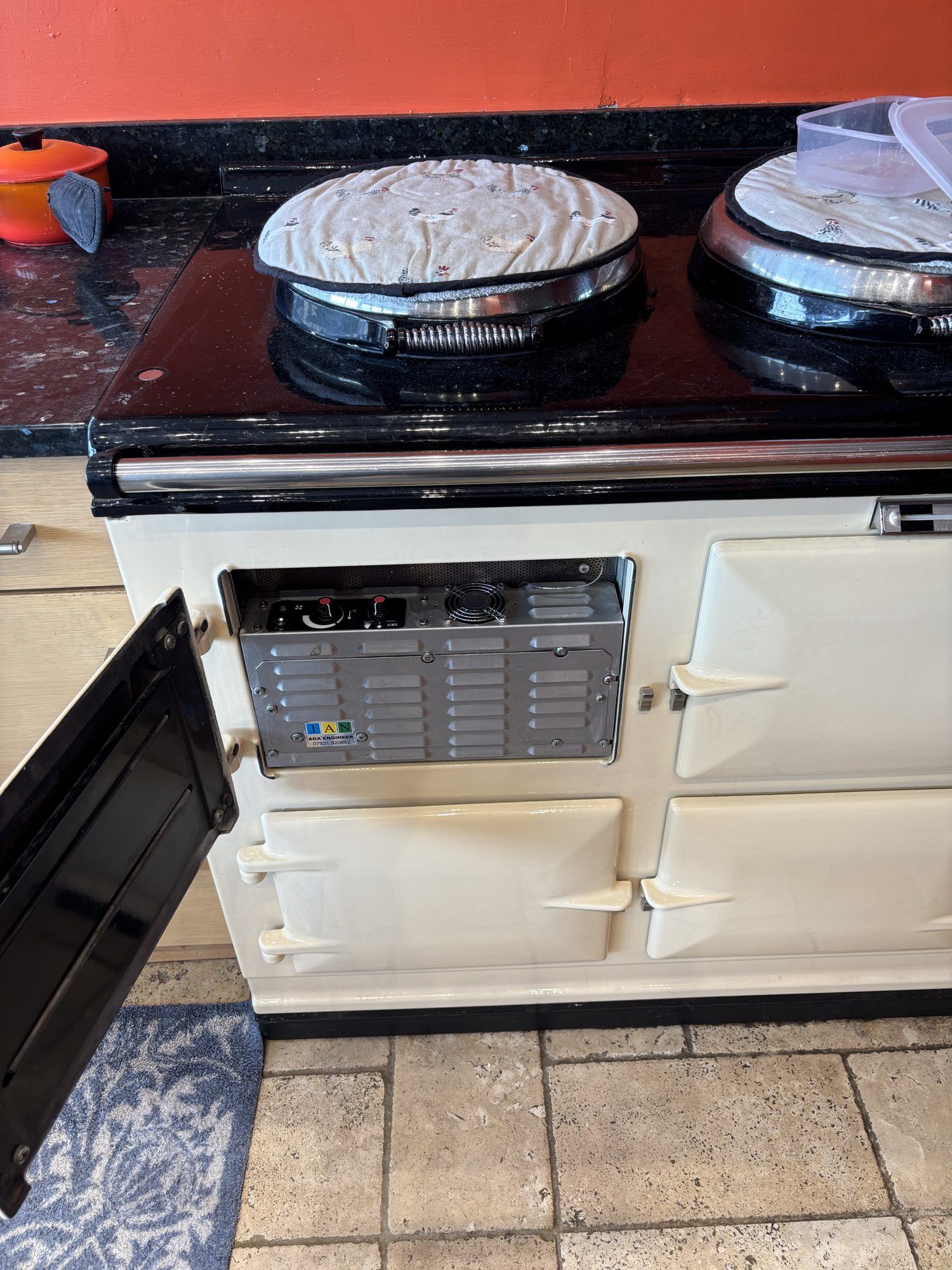A cream 13 amp electric AGA with the top left door open, showing the AIMS control panel and its cooling fan