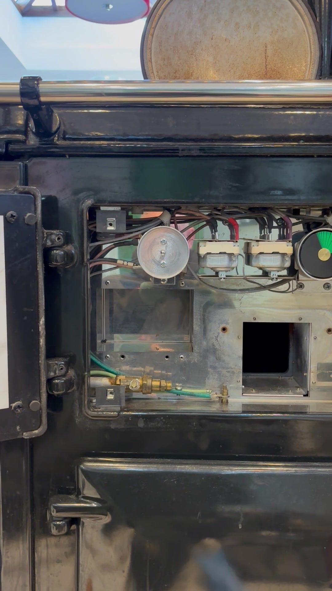 A black gas AGA DC3 with its burner door open, showing the wiring, thermostats and brass gas fittings inside
