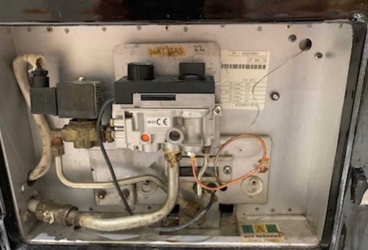 The burner compartment of a natural gas AGA with its door open, showing the gas valve, the pipework and the wiring
